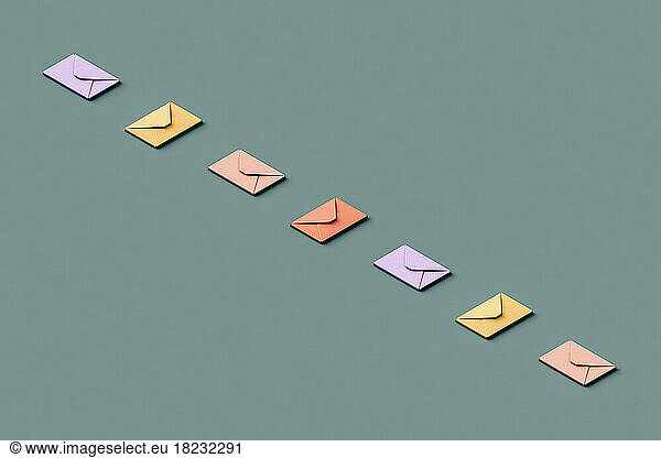 Three dimensional render of row of pastel colored envelopes flat laid against green background