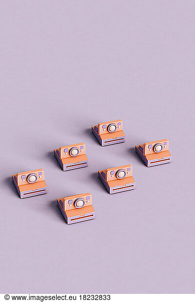 Three dimensional render of rows of instant cameras flat laid against purple background