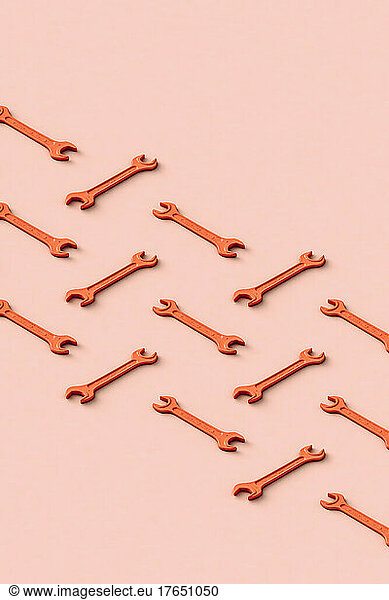 Three dimensional render of rows of orange colored wrenches flat laid against beige background