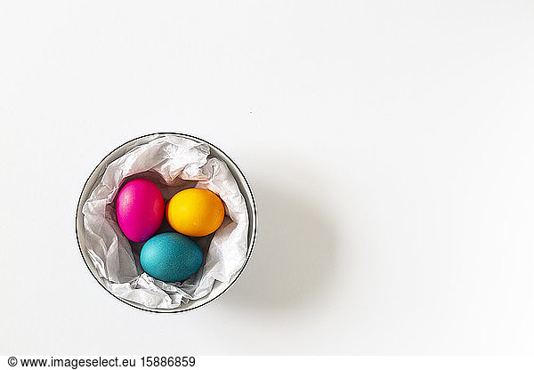 Three dyed Easter eggs in a bowl on white bachground