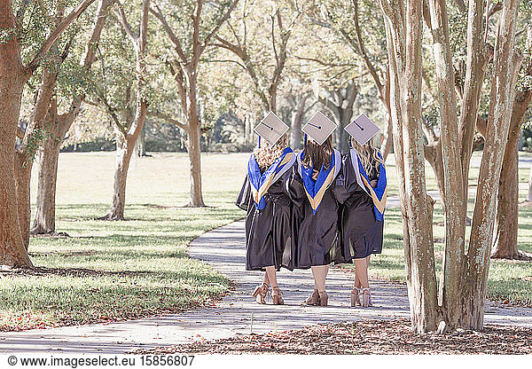 Three friends in graduation caps and gowns on path arms around waist