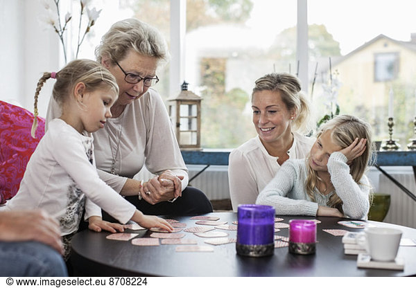 Three generation females playing card puzzle game at home