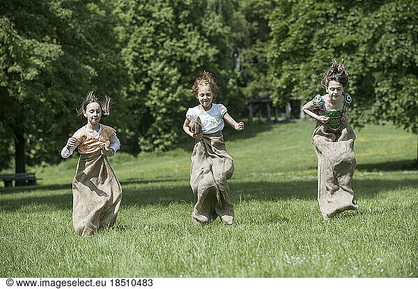 Three girls jumping in sack race in a field  Munich  Bavaria  Germany