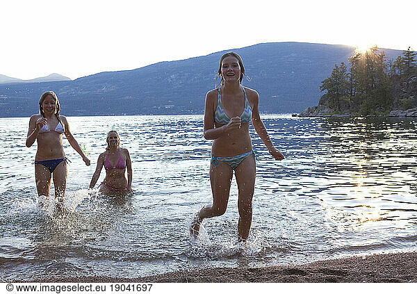 Three girls run out of lake at sunset