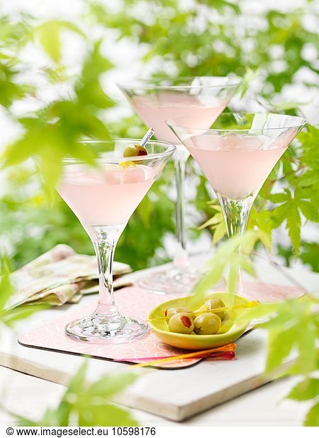 Three glasses of pink grapefruit and martini cocktails with green olives