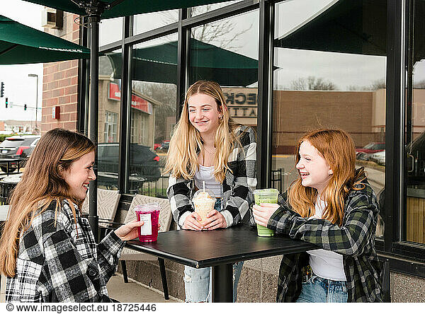 Three happy teen girls having drinks outside a coffee shop.