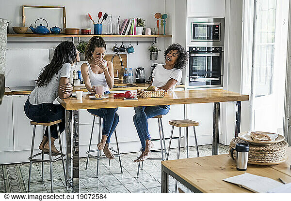 Three happy women sitting at kitchen table at home socializing