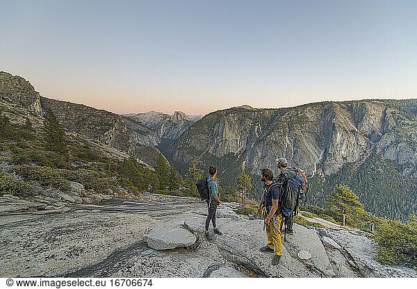 Three hikers looking at Half Dome from El Capitan sunset Yosemite