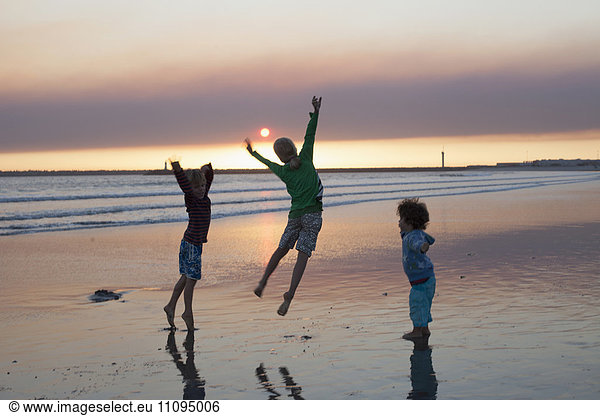 Three kids jumping on beach during sunset  Viana do Castelo  Norte Region  Portugal