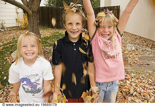 Three kids  two girls and one boy  play in the fall leaves in Fort Collins  Colorado.