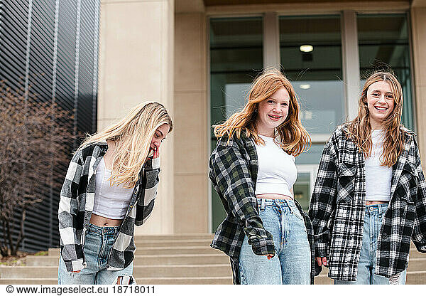 Three laughing teen girls outside together on stairs.