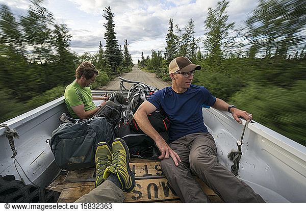 Three men hitch hiking in the back of a pick up truck in Alaska