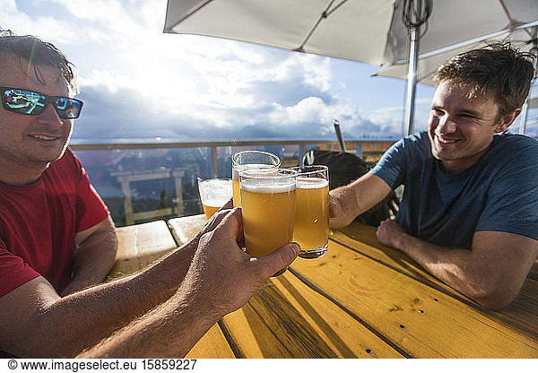Three men toast their beers on restaurant patio