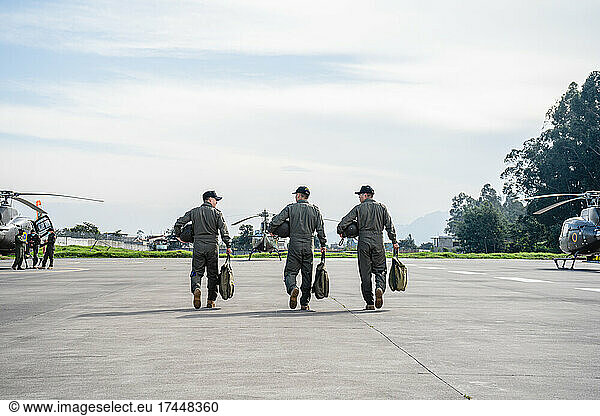 three military men walking on a runway towards the helicopters