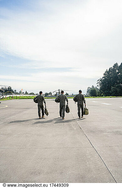 three military men walking on a runway towards the helicopters