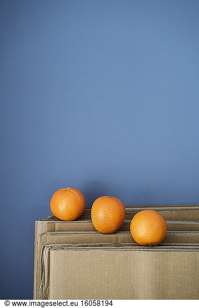 Three oranges on cardboard against blue wall