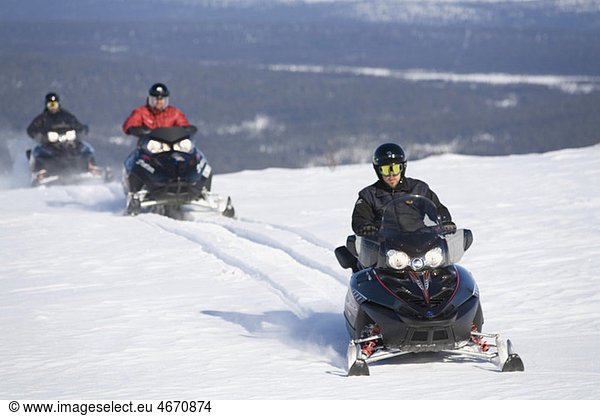 Three people driving snowmobile