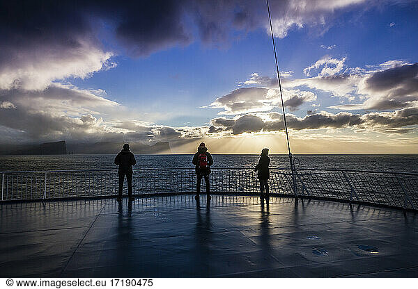 Three people enjoy the sunset on the boat deck as it leaves to Iceland
