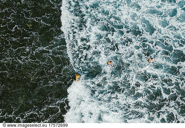 Three people playing in the waves of the ocean from a drone