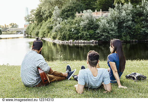 Three people relaxing in park with guitar