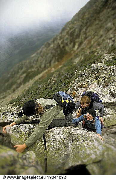 Three people scramble their way across a mountain.