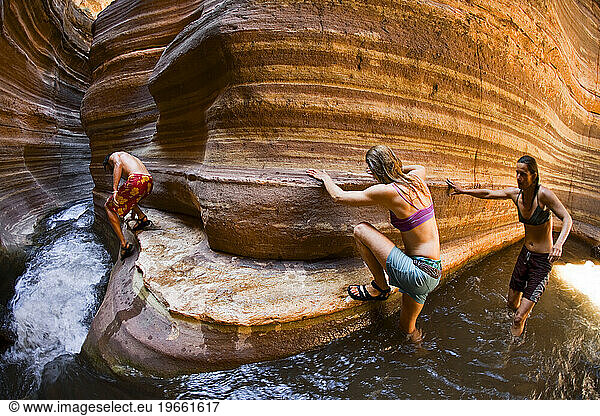 Three people scrambling down a slot canyon with flowing water  Deer Creek  Grand Canyon  Arizona.