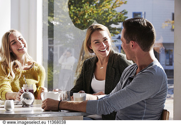 Three people sitting at a table talking  with mugs and jars of smoothies.