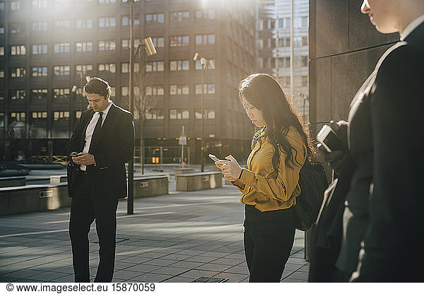 Three people standing in square using smartphones