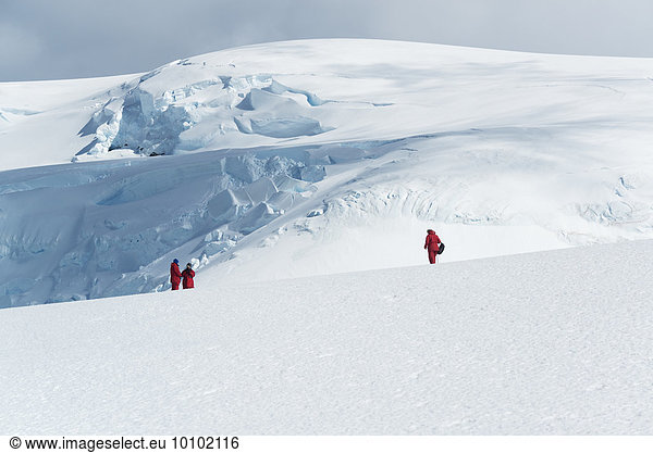 Three people standing on the ice in front of a mountain covered in ice and snow.