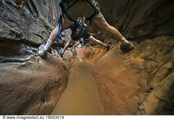 Three people stemming between two walls above water in slot canyon  Utah.