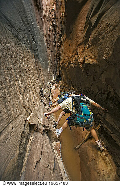 Three people stemming between two walls above water in slot canyon  Utah.
