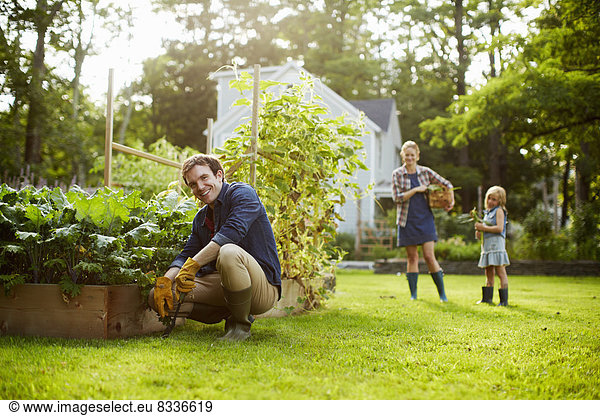 Three people  two adults and a child in a vegetable garden.