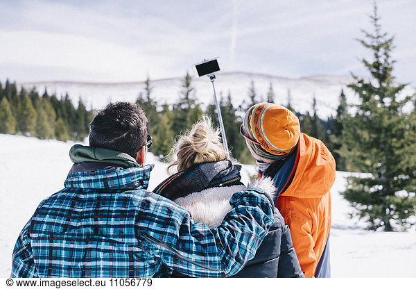 Three people  two men and a young woman in skiing gear posing for a selfie  one holding a selfie stick.