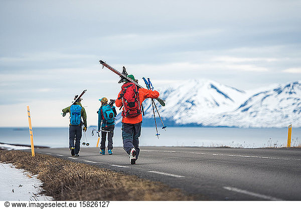Three people with skis walk down a road in Iceland