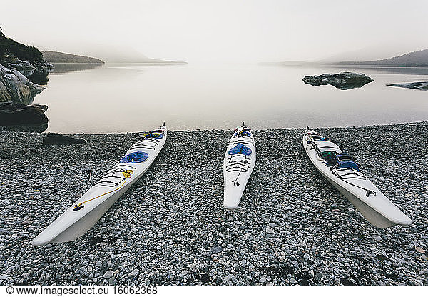 Three sea kayaks pulled up into shoreline of secluded cove in Muir Inlet overcast sky in distance Glacier Bay National Park Alaska