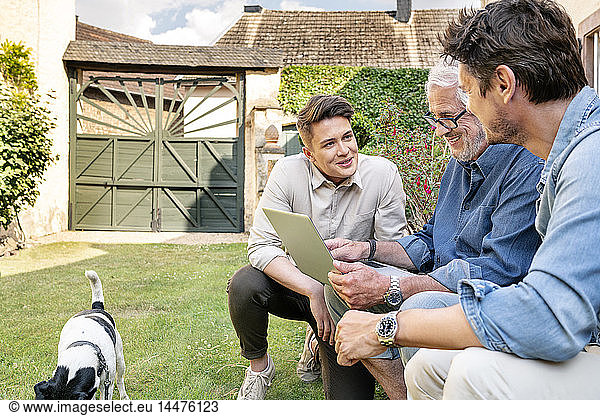 Three smiling men of different age using tablet in garden
