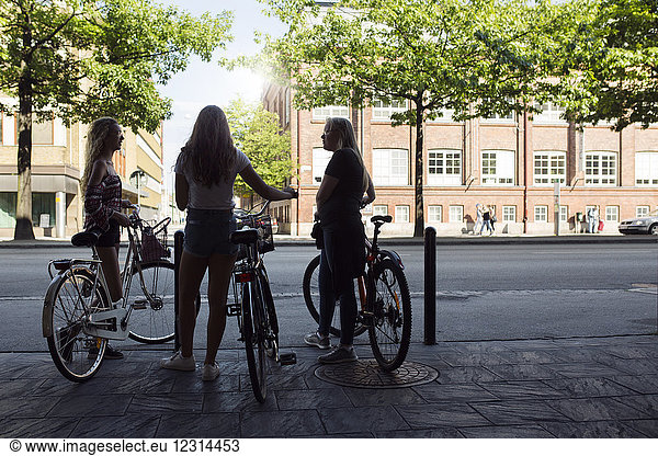 Three teenage girls (14-15) on bicycles talking