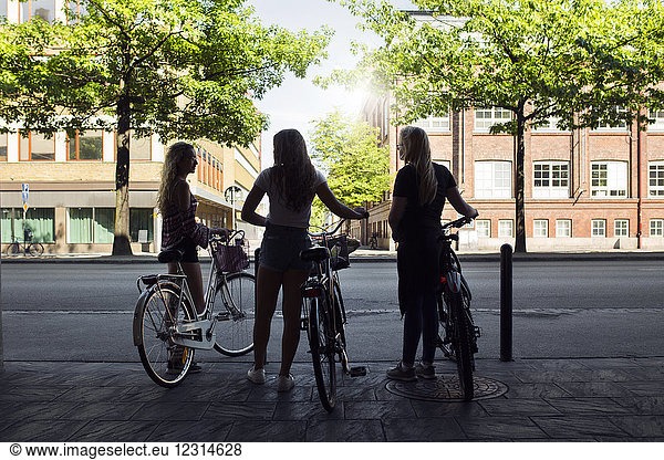 Three teenage girls (14-15) on bicycles talking