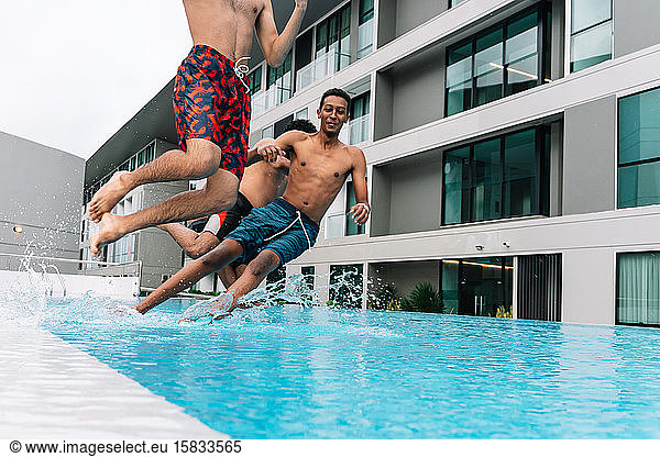 Three teenagers jumping into a pool surrounded by buildings