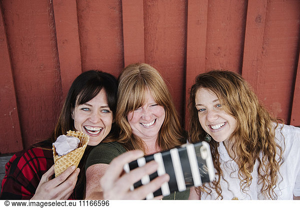 Three women eating ice cream  taking a selfie with a cell phone.