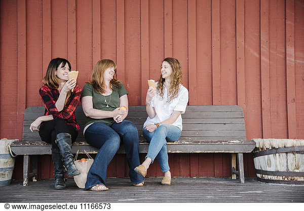 Three women sitting on a bench  eating ice cream.