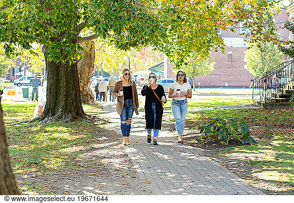 Three women walking down Main Street drinking coffee