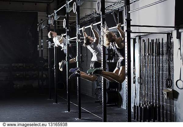 Three young adults training on wall bar in gym