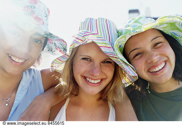 Three young girls in a row wearing sunhats looking at the camera and smiling.