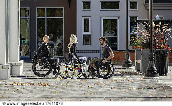 Three young paraplegic friends spend time together talking outside on a walkway in a city area; Edmonton  Alberta  Canada