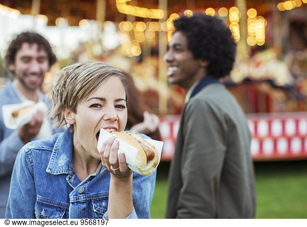 Three young people eating hot-dogs in amusement park