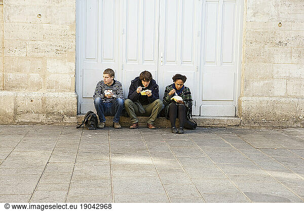 Three young people eating while sitting on a step.