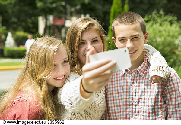 Three young people  two girls and a boy  posing and taking selfy photographs.