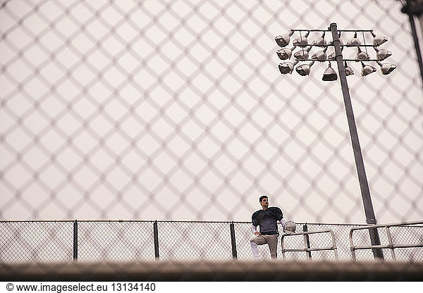 Tiefblick auf einen durch den Zaun gesehenen American-Football-Spieler  der im Stadion steht und weg schaut