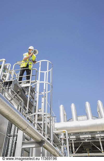 Tiefblick auf einen Ingenieur  der ein Megaphon in einem geothermischen Kraftwerk benutzt